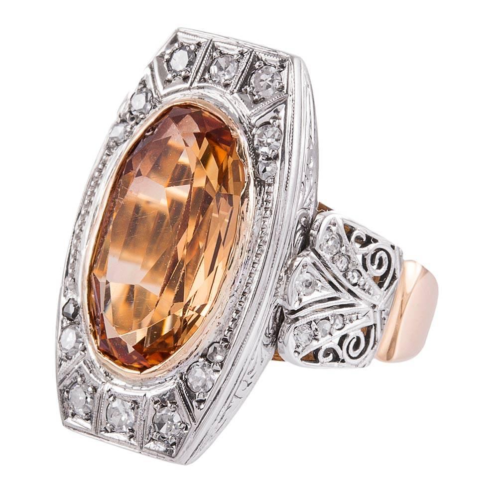 Made of 9 karat white and 15 karat yellow gold, the detailed filigree mounting contains a large faceted oval bezel set Imperial topaz. The precious gemstone weighs approximately 6 carats and displays beautiful, intense persimmon color. It is framed