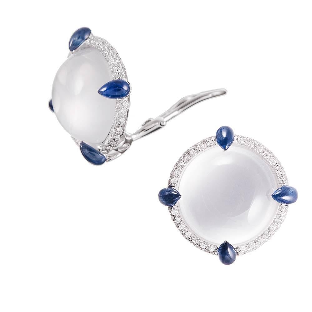Measuring just hint under 1 inch in diameter, the earrings are designed as a large cabochon of white quartz, framed in brilliant white diamonds and tipped with blue sapphire "prongs". The quartz is an alluring, mystical stone that is