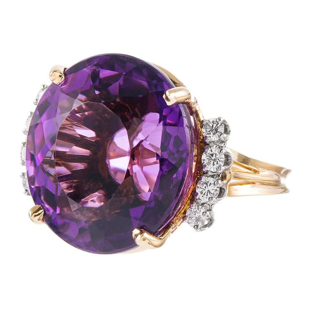 18 karat yellow gold frame containing a striking faceted round amethyst weighing 25 carats. The color is luscious and rich- a true jewel tone. Accented with four round diamonds on each side, adding a pop of brightness to the design. Size 7.25 can be