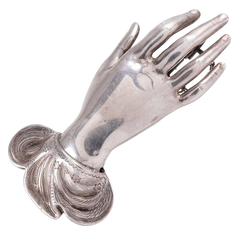 A unique adornment, measuring an assertive 3 inches long and 1.5 inches wide, the silvered lady's hand with long, elegant fingers, her worst adorned with an embellished sleeve. Dated 1848. Hallmarked on the back and fitted with a barrel pin clasp