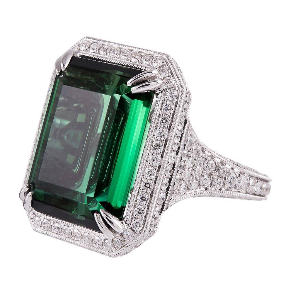 18k white gold ring set in the center with a 13.22 carat emerald cut green tourmaline and framed in an elaborate diamond mounting. Look closely to notice the striking architecture of the setting, with diamonds set at every opportunity and a unique