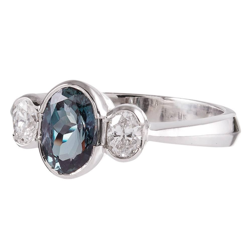 An uncommon gemstone for the appreciator of rarities, this 1.40 carat alexandrite is perfectly accented with a pair of oval diamonds that weigh .30 carats combined. Set in a clean platinum bezel setting. The major stone is accompanied by a GIA