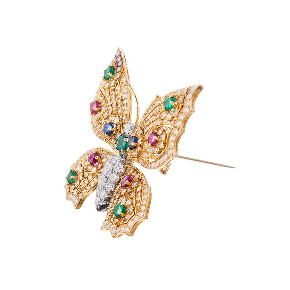 A striking butterfly brooch, glittering at every opportunity with brilliant white diamonds and intense flashes of color from colored gemstones. Measuring 1.75 inches square, this piece offers an impactful aesthetic with hints of playfulness and