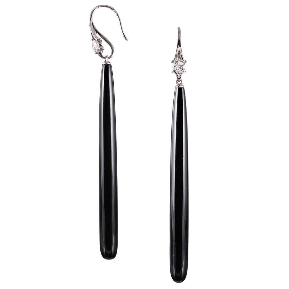 A dramatic pair of onyx torpedo earrings, measuring nearly 4 inches in total length. Smooth, sleek teardrop-shaped onyx drops are suspended from substantial 18k white gold ear wires and decorated with a solitary diamond. The round brilliant stones