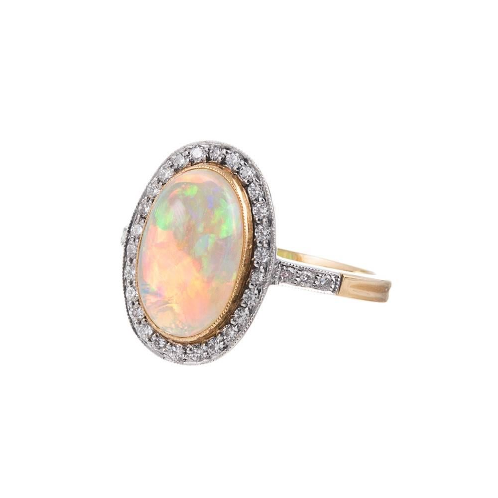 The elegant 2.23 carat oval cabochon opal is set in a delicate bezel of 18k yellow gold and finished with millegrain. The stone is further enhanced by a frame of brilliant white round diamonds that weigh .28 carats in total and are set in 18k white