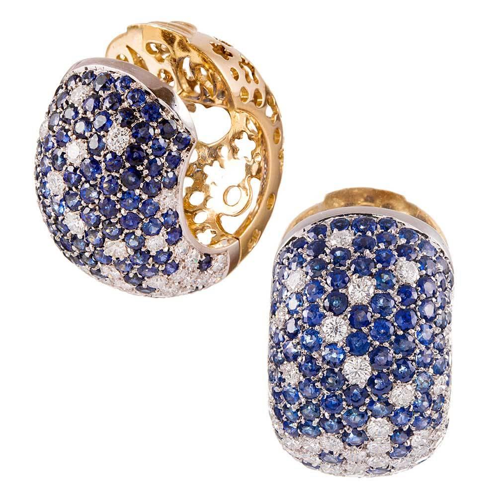 Classic, with a twist, these 18k yellow gold earrings are designed as a timeless hoop style and set with brilliant round white diamonds and royal blue sapphires- 2.80 and 5.50 carats respectively. The three-dimensional look appears substantial and