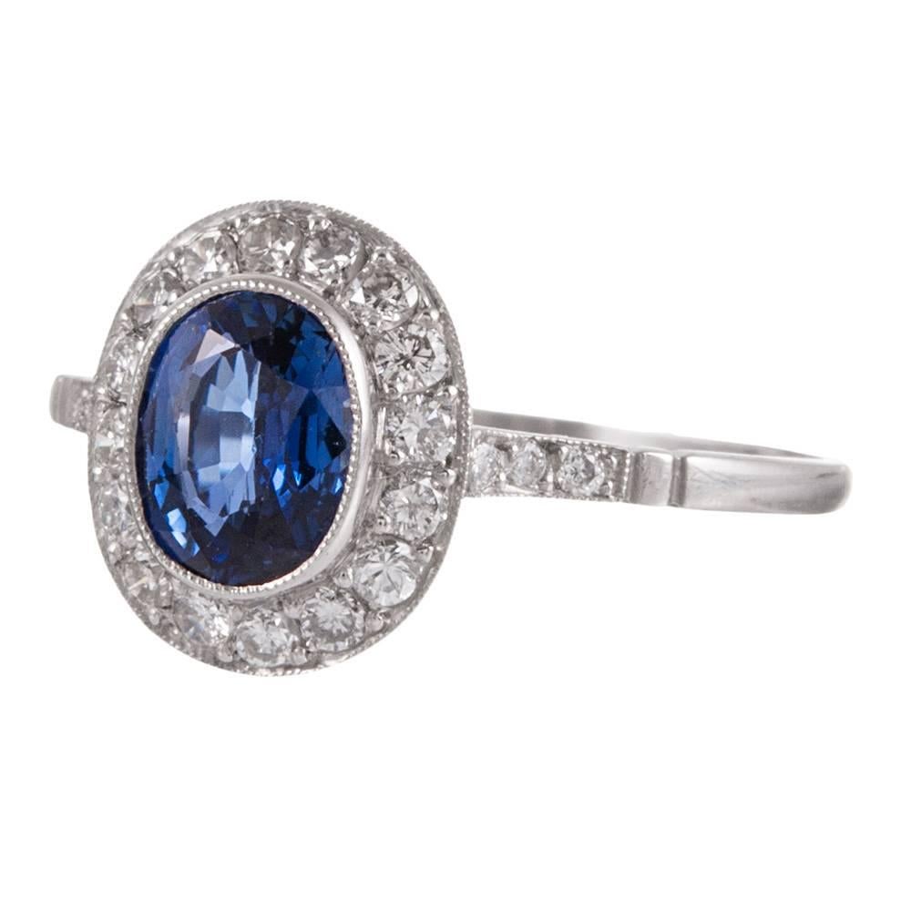 Created in the classic art deco style, yet of more modern age, this sweet platinum ring has a 1.14 carat faceted oval sapphire center, framed with a border of diamonds and accented with diamonds on the shoulders. Note the hand created filigree