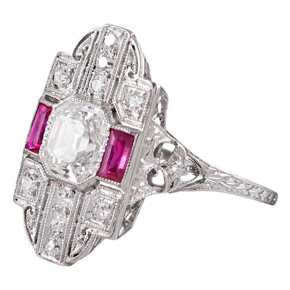 A charming bit of genuine art deco finery, the platinum ring is set in the center with a 1.05 carat asscher cut diamond, then framed by an ornate architectural backdrop of rubies, diamonds, hand engraving and mille grain. This style has a striking