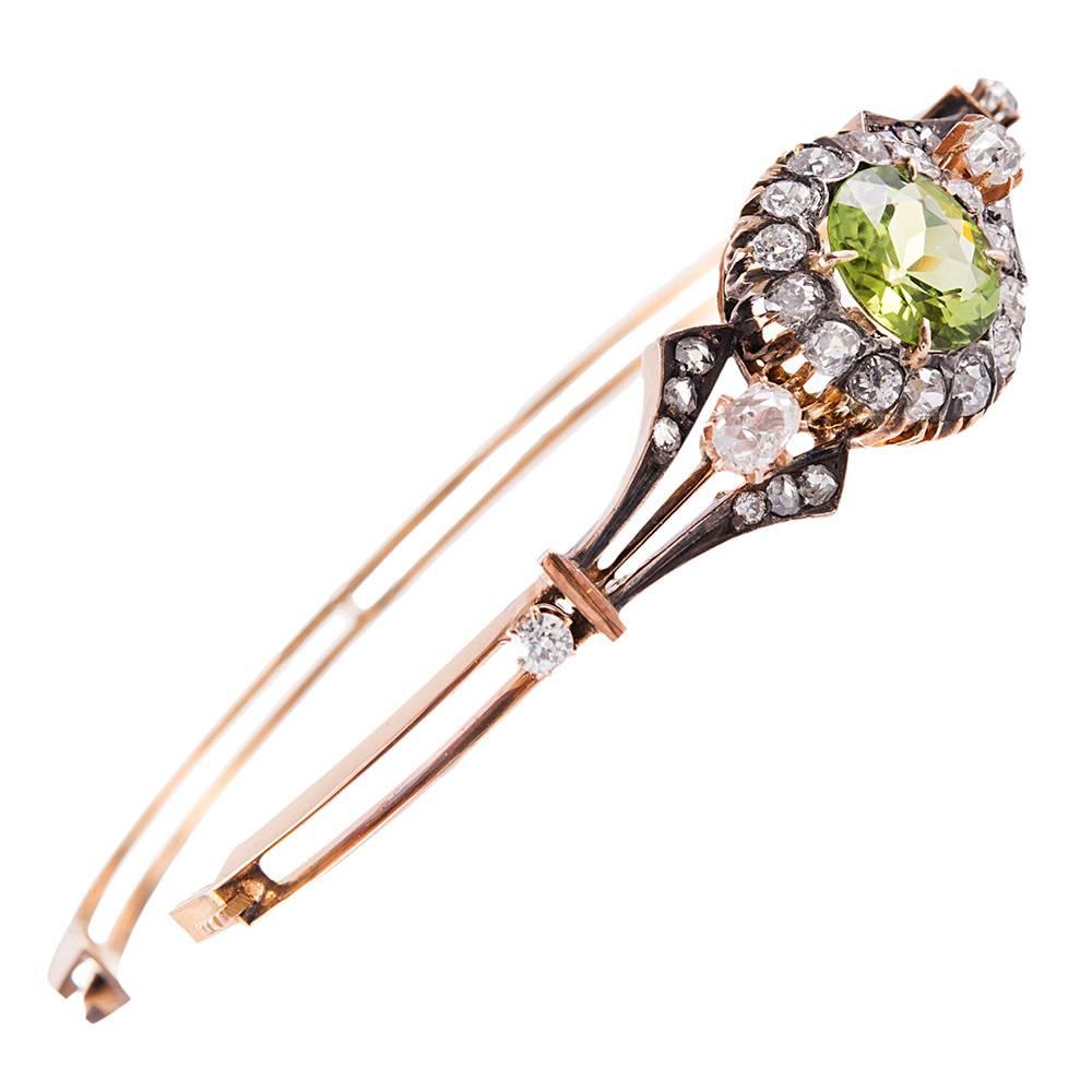 A 3.75 carat faceted round peridot is framed by a symmetrically-assembled border of old mine- and rose cut diamonds. The 15 karat rose gold oval frame has an interior diameter  of 2 3/8 by 2 inches interior diameter. Note the lovely pair of oval old