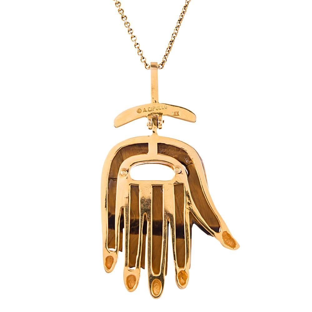 A chic means of warding off evil spirits, this Hamsa pendant is carved of tiger's eye, set in 18k yellow gold and signed "A. Cipullo", measuring 2 by 1.25 inches. It is suspended from a 25 inch antique chain. The chain is not signed, but