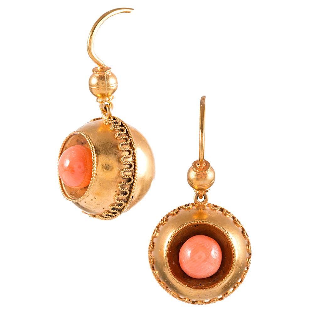 Darling orbs of 18k yellow gold with textured edges contain a polished coral bead. Nestled in a rounded crevice, the bright pop of color offers a cheerful burst from its golden backdrop. The earrings measure just over an inch long.
