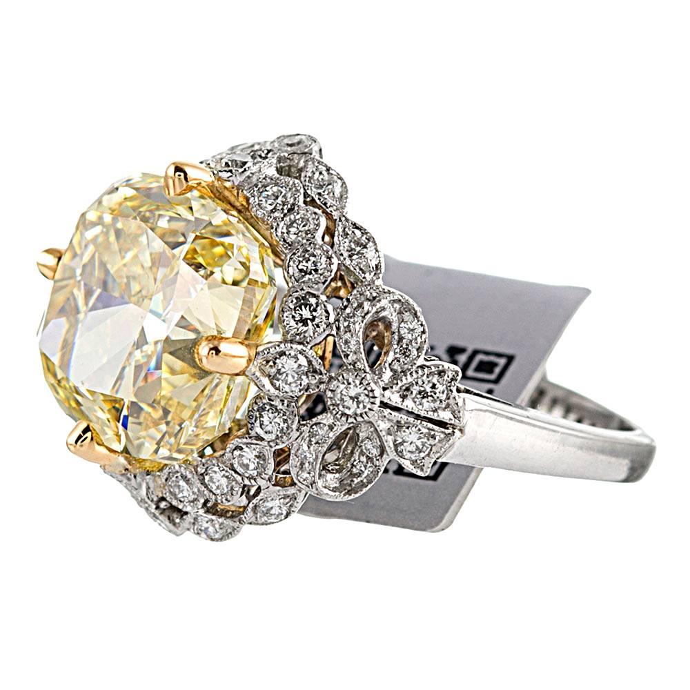 Ultra-feminine charm is reflected in this striking ring. At the center of the platinum Edwardian-inspired mounting is a 7.80 carat cushion cut diamond, set in 18k yellow gold prongs, that sits nestled in an elaborate vintage style nest of brilliant