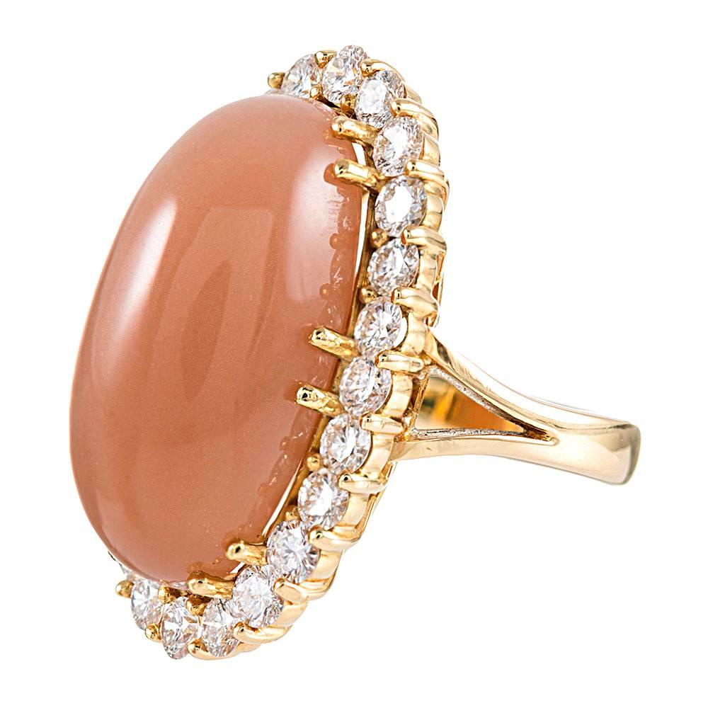 An elegant design, with an elongated oval cabochon cut moonstone framed in white diamonds, the feminine shape and natural color hues will look well with any palette. The moonstone exhibits a tangerine color that is alluring and a bit mystical, while