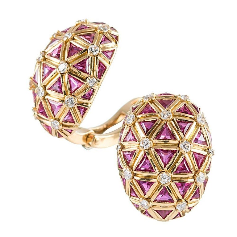 Three-dimensional half oval orbs with a honeycomb pattern assemble din 18k yellow gold are set inside each nook with a triangular pink sapphire and decorated with brilliant white diamonds. The intense color of the sapphires nearly resembles that of