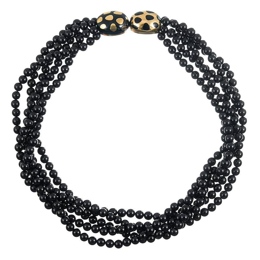 Measuring 17.5 inches in overall length, the necklace is designed as five strands of polished 6mm onyx beads, connected by an opposing pair of 18 karat yellow gold and black enamel ovals. The clasp can be worn off to one side, allowing display of