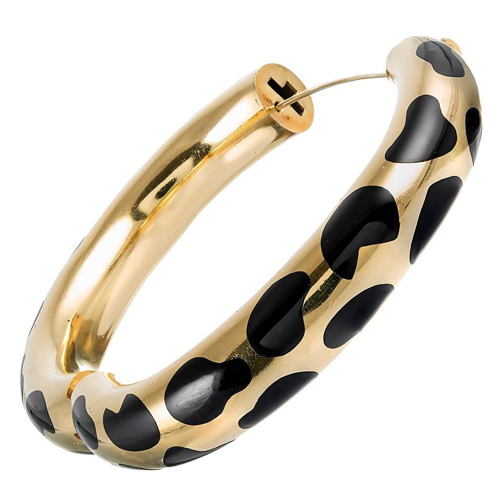 The three-dimensional bangle is rendered in 18 karat yellow gold and spotted with a pattern of black enamel. The interior diameter is 2.25 by just under 2 inches. The piece opens with a single hinge and is secured by an interior concealed safety.