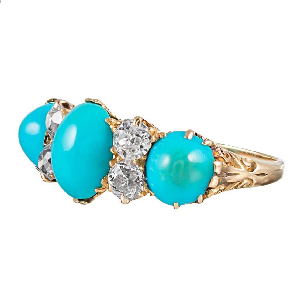 The classic English carved ring is a hallmark of Victorian jewelry. This piece is made of 18 karat yellow gold and set with three cabochons of turquoise with double stacks of old European cut diamonds between. The diamonds weigh approximately .75