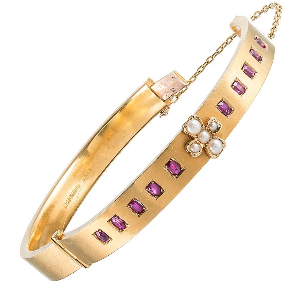 Faceted rectangular rubies are set into a bangle of 15 karat yellow gold, with a cluster of pearls fashioned into a cross or four-leaf clover shape anchored in the center. The interior diameter measures 2.25 by just under 2 inches and the piece is