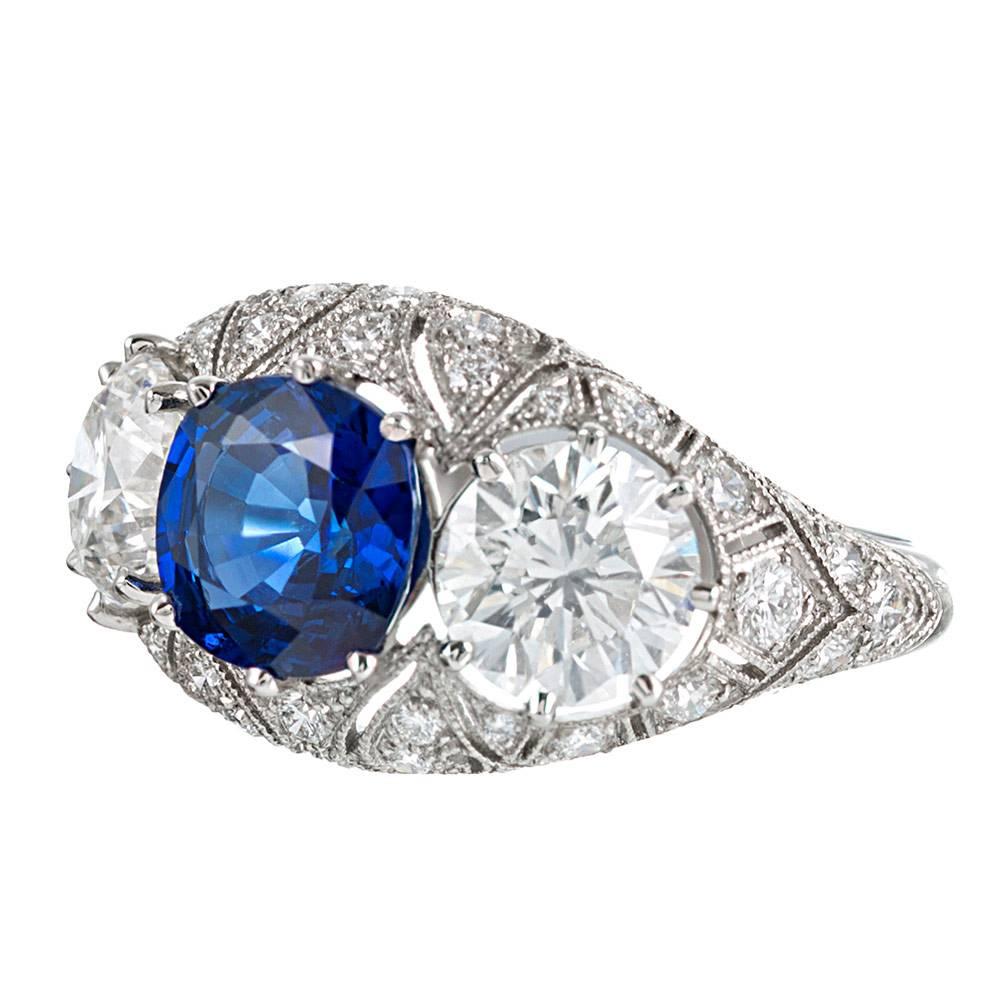 A brilliant combination of art deco inspiration and modern hand-craftsmanship, this platinum mounting is adorned by forty diamonds that weigh .68 carats combined and further accented by scrolling open filigree and mille grain. The center sapphire