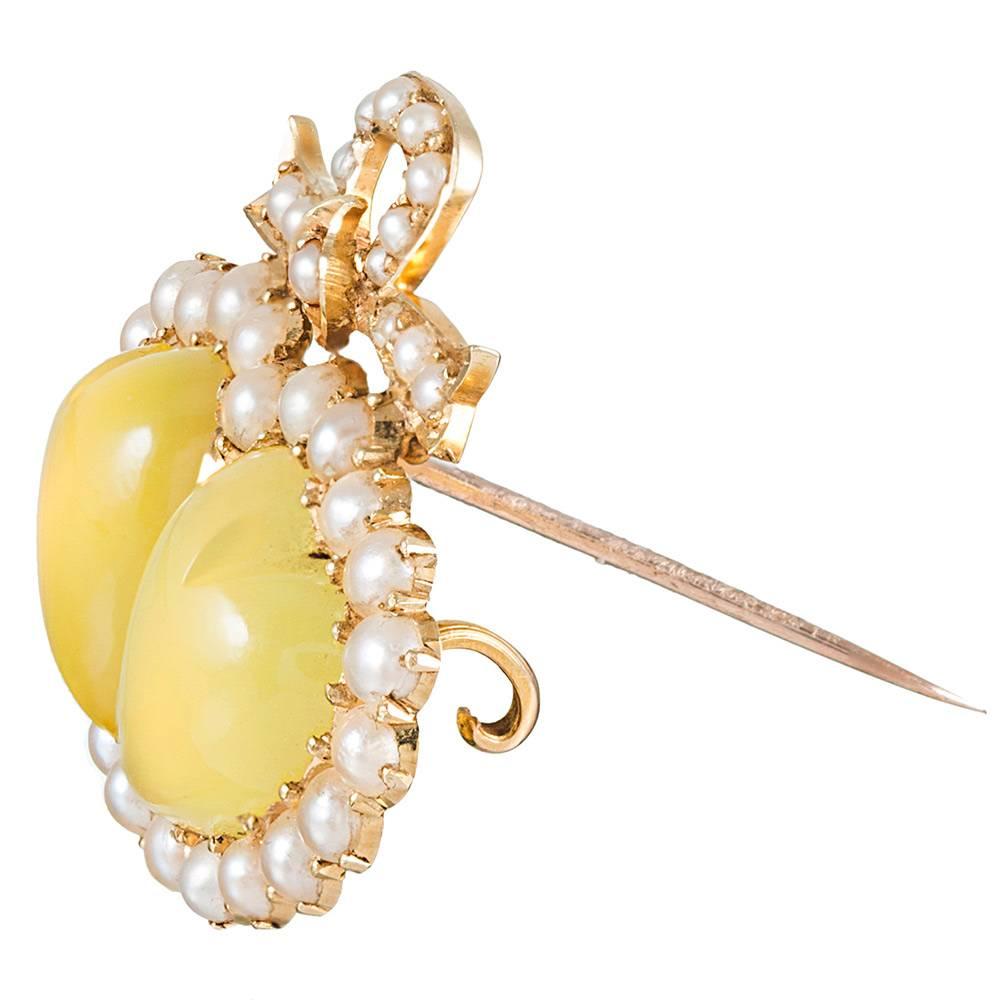 A charming rendering of this classic Victorian motif, the unfaceted chrysoberyls burst forth from their pearl frames with alluring color and shape. Made of 15 karat yellow gold and measuring 1 ¼ by 1 1/8 inches, this adorable relic will charm those