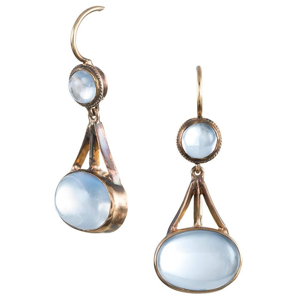 Early American moonstone earrings created during the “arts & crafts” period, circa 1915. An oval cabochon of blue flash moonstone is suspended from an architectural bridge of 14k yellow gold and topped with a smaller round cabochon. 1.25 inches long.