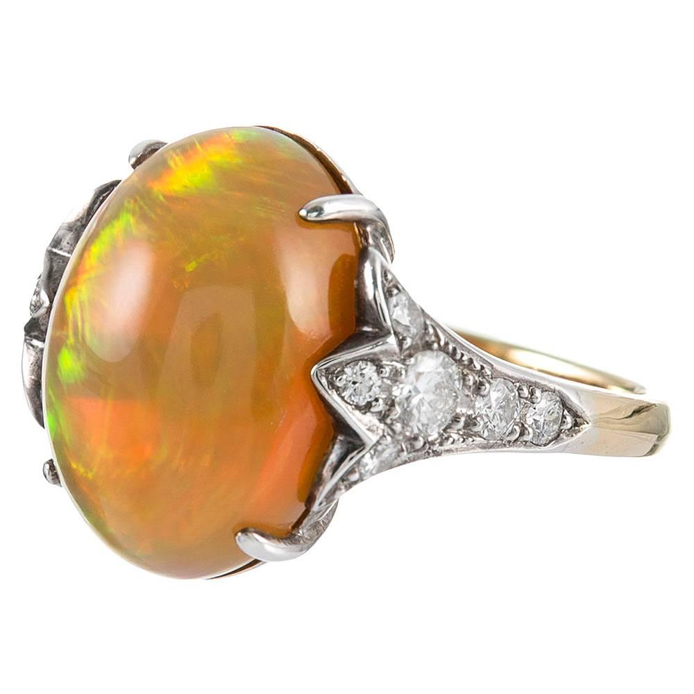 An exotic and beautiful Mexican fire opal cabochon of 8 carats is flanked by a tulip-shaped cluster of diamonds. The opal exhibits strong flashes of green, red and yellow against its vibrant orange background. Made of platinum and 18k yellow gold.