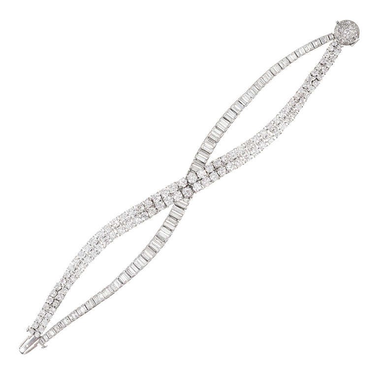 Platinum bracelet, designed to appear as though you are wearing a pair of bracelets, crossed over one another. One section contains a row of graduated baguette diamonds and the other a double row of graduated round diamonds. The sections come