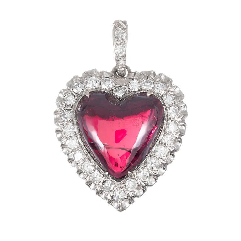 14k white gold pendant front the 1940s with a cabochon cut garnet heart, surrounded by white diamonds and finished with a diamond bale. The vintage character of this piece lends a special charm to this classic style. 1.25 inches.