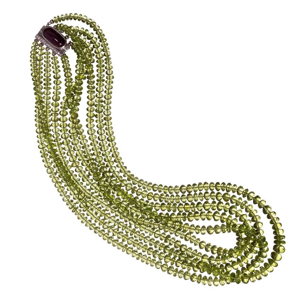 Five strands of peridot beads, an impressive 985 carats in total, with graduated lengths from 17 to 21 inches are fashioned together to create this unique adornment. The strands of peridot beads are gathered and suspended from an asymmetric 18 karat