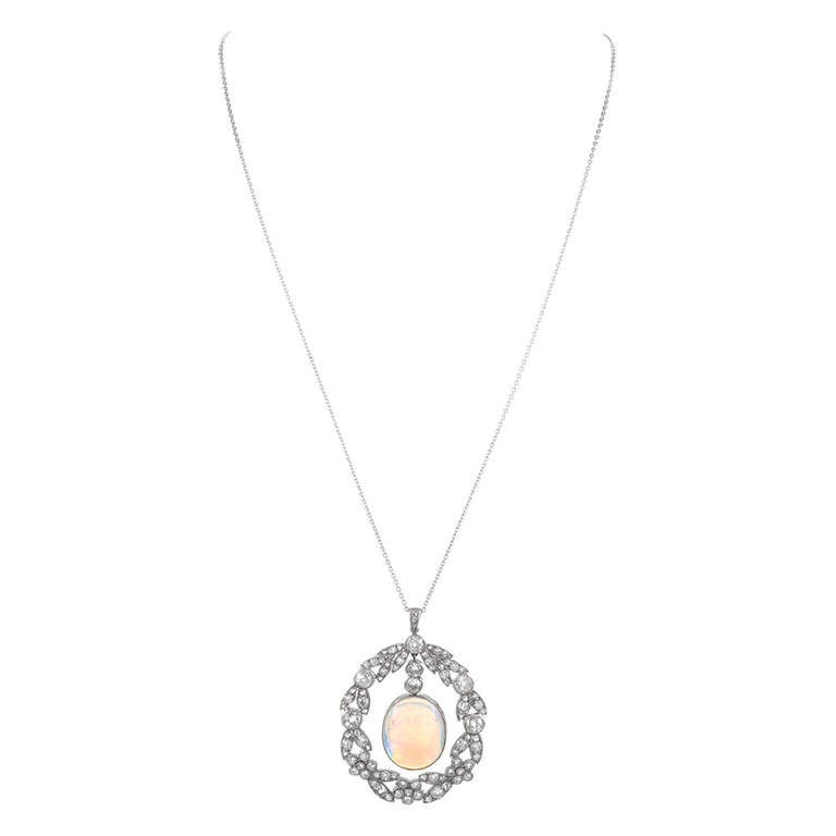 Ornate art deco platinum pendant, large for the period and displaying an 8 carat oval opal, suspended from a frame of bezel-set diamonds. The diamonds are configured in a flower pattern, creating the look of a wreath with the opal at the center. In