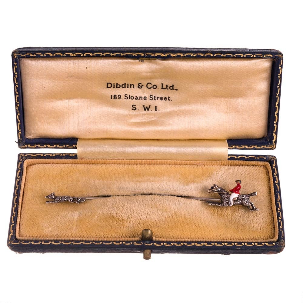 Yellow gold and silver jabot pin, depicting an enameled hunter on rose cut diamond-studded horseback, chasing a rose cut diamond fox. The pin measures 3 inches long and is offered in its original antique presentation box.