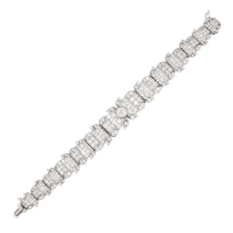 An undulating design of platinum scrolls that almost looks like diamond-studded curls of heavy ribbon, gently tapered in width from front-to-back and set in the center with a 1.25 carat brilliant white diamond. An additional 9 carats of diamonds are