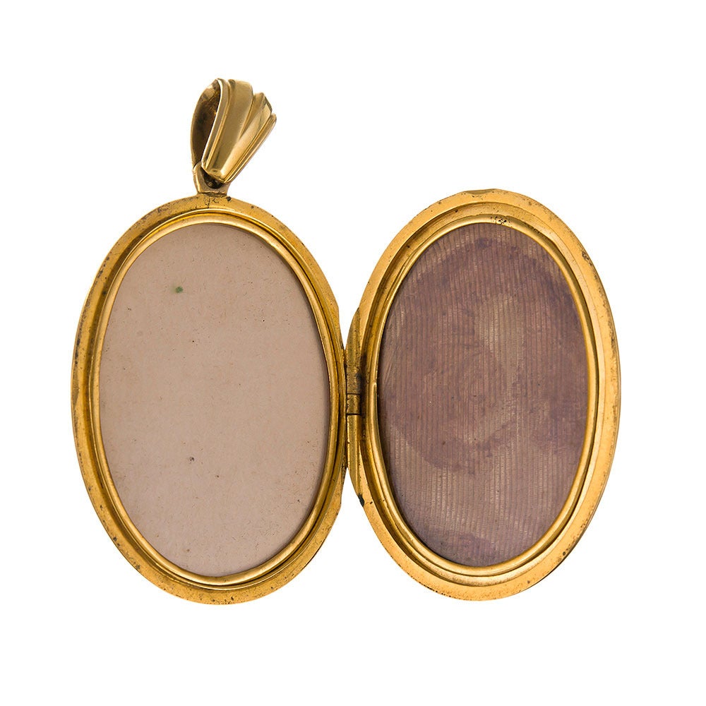 18k yellow gold pendant, substantial size, measuring 2.5 by 1.25 inches, and set with a cabochon garnet, framed by pearls and a starburst design of cobalt blue enamel. The single hinge design has room for relics or photos in both sideband still