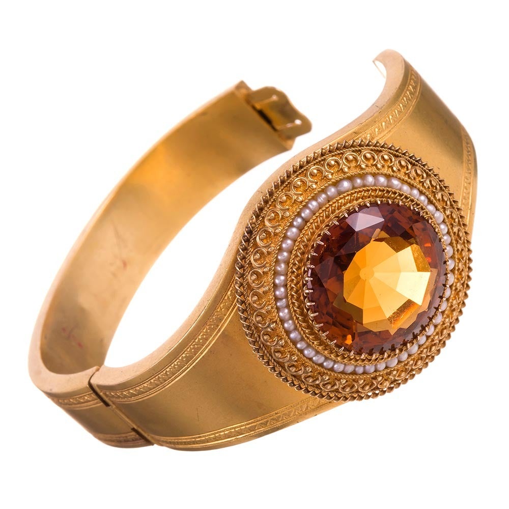 18k yellow gold bangle, single hinge design, set in the center with a 25 carat faceted round citrine. The major stone is framed in multiple layers of intricate Etruscan granulation, with scrolling gold wire and a filigree pattern. It is further