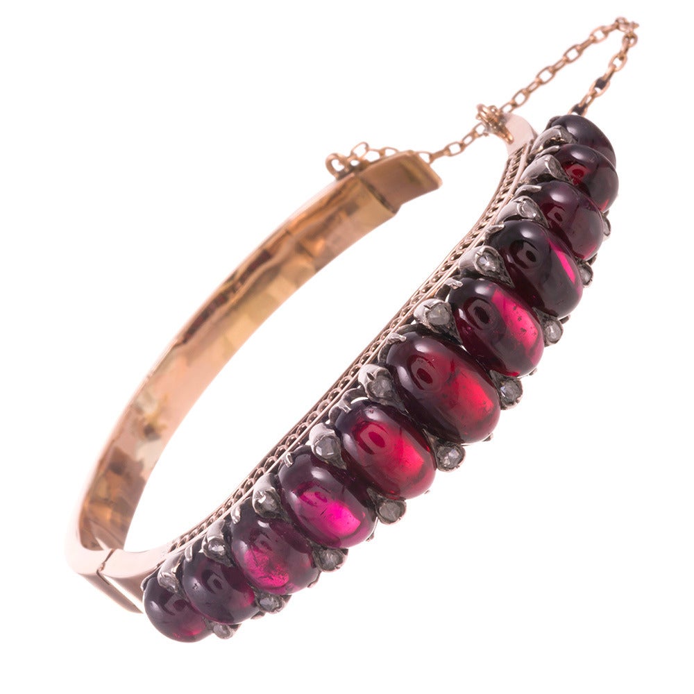 18k rose gold and silver Victorian bangle, set with an impressive row of cabochon garnets, approximately 40 carats in total, gently graduated in size and peppered with rose cut diamonds. The diamonds are set in teardrop-shaped silver bezels that fit