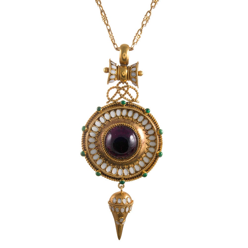 18k yellow gold sculptural pendant, almost Aztec in its rendering, but distinctly Etruscan in design, set in the center with a cabochon garnet and framed by crisp white enamel and green enamel dots at the “hour markers”. A stylized bow tie shaped
