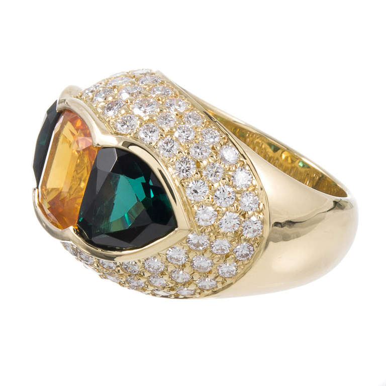 The striking color combination makes a sophisticated statement.  A 4.50 carat GIA-certified yellow sapphire is flanked by 7 carats of green tourmaline and outlined in a polished golden bezel. Approximately 2.70 carats of brilliant round diamonds