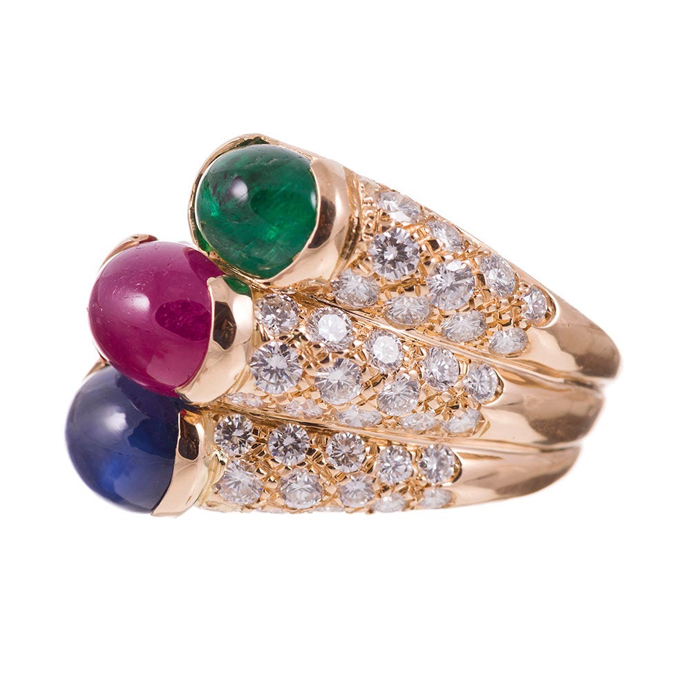 18k yellow gold ring designed as a fanned stack of three bands, each set with brilliant round diamonds and a cabochon gemstone centerpiece. The emerald weighs 1.75 carats, while the sapphires weighs 1.70 and the ruby approximately 2.00 carats. The