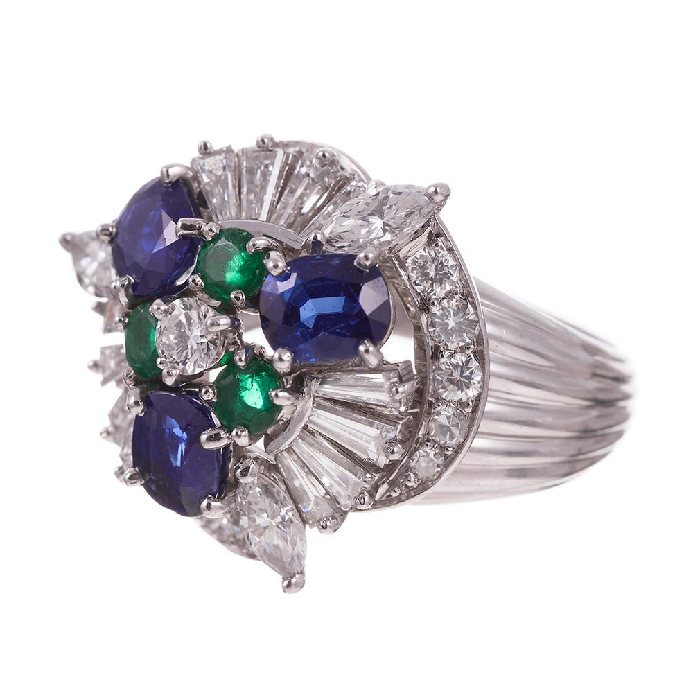 Platinum cluster ring set with brilliant round, marquis and tapered baguette cut diamonds (2.50cttw), faceted oval blue sapphires (1.50cttw) and round brilliant emeralds (.30cttw), assembled in a unique design that is decidedly mid-century. The