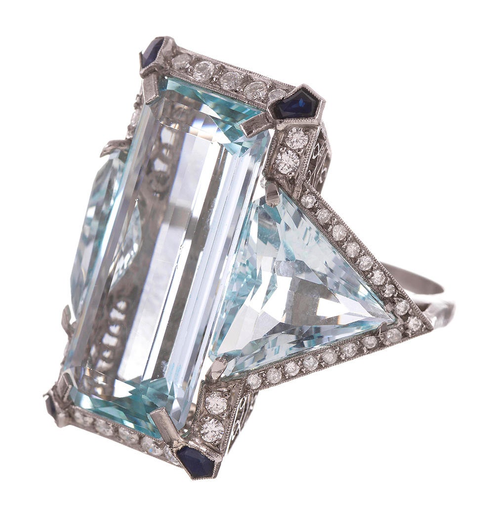 Forged by hand of platinum and set with a large rectangular aquamarine flanked by trillion aquas, the four corners dotted with blue sapphires and the edges trimmed in brilliant diamonds. The talon-like prongs lay outstretched over the corners of the