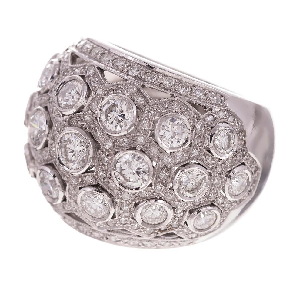 18k white gold dome ring, designed as a pattern of hexagonal bezels speckled with diamonds and set with larger brilliant diamonds in their centers. An additional row of diamonds borders the edges. This ring ha s a striking presence, yet a flat and