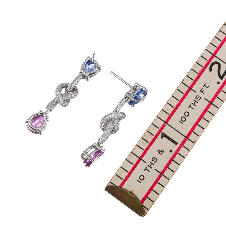 Sweet and feminine, with beautiful colors, a showcase of opposing sapphires, connected by a diamond knot. Measuring just 1.25 inches in length, these earrings will add a special splash for every day! 18k white gold. The sapphires weigh 6.30 carats