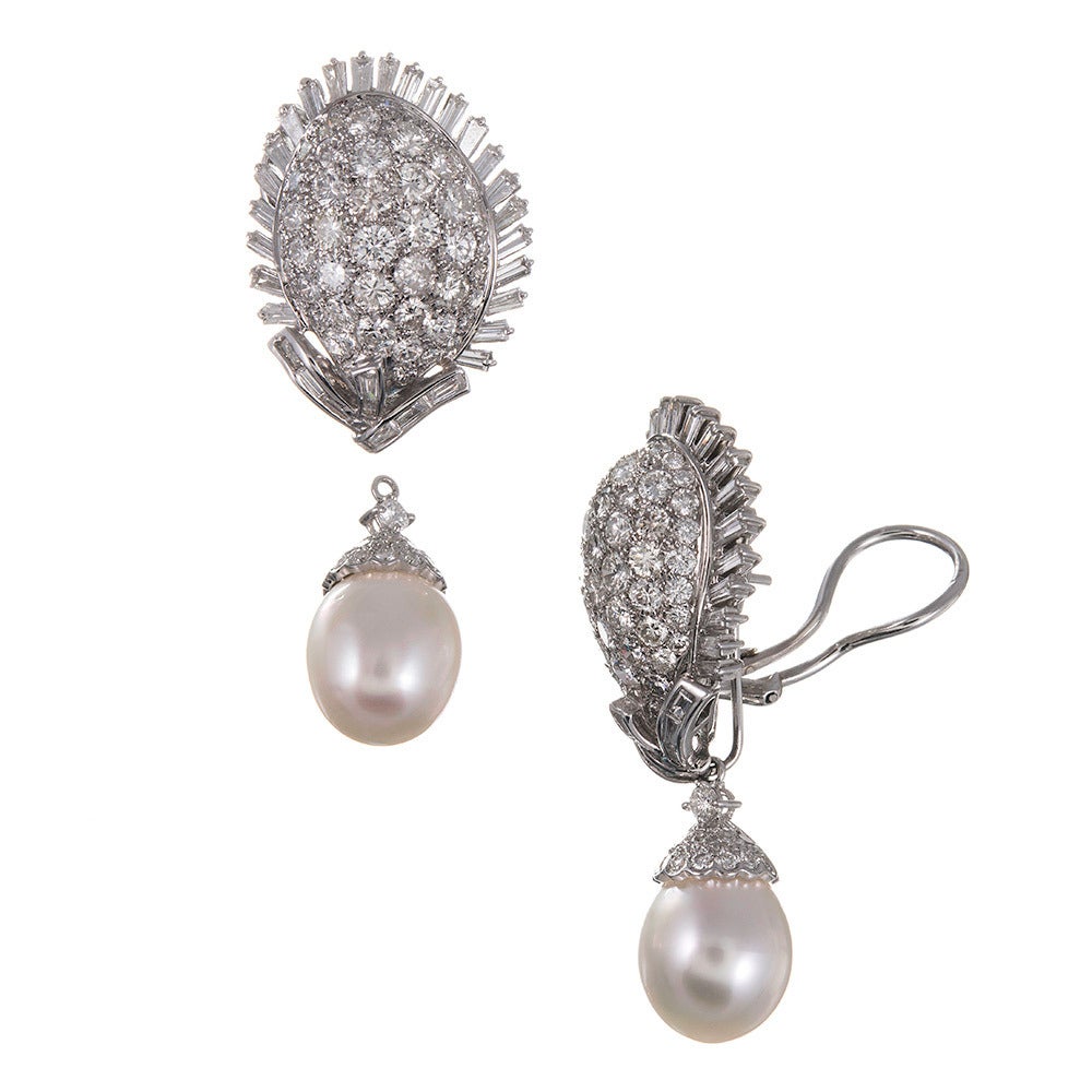 18k white gold earrings, a modified cluster style in a mid-century distinct egg shape, framed in a burst of baguette diamonds and punctuated with a substantial pearl drop. The pearl is a removable enhancer that adds extra length, movement and the