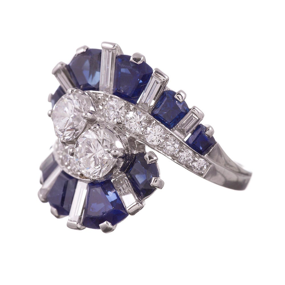 This ring combines multiple design elements into one, compliments of esteemed designer Oscar Heyman. Rendered in platinum this is a cocktail, cluster, ballerina and a bypass ring set with 4.26 carats of custom cut blue sapphires and 2.65 carats of