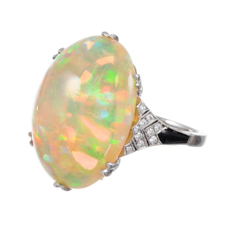 Platinum ring, a modified crown design, with diamond-studded split prongs supporting an 11 carat cabochon cut opal. The major stone exhibits wonderful play of light, with strong green and yellow and bright flashes of red. Hints of onyx in the