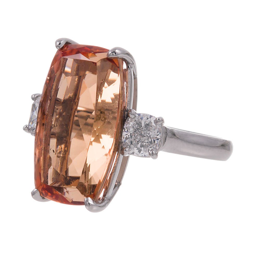 Gleaming from its hand fabricated platinum mounting, this super fine gem Imperial Topaz is seated between a pair of brilliant cushion white diamonds. The elongated shape of the major stone sits elegantly on the finger, enhancing the feminine charm.