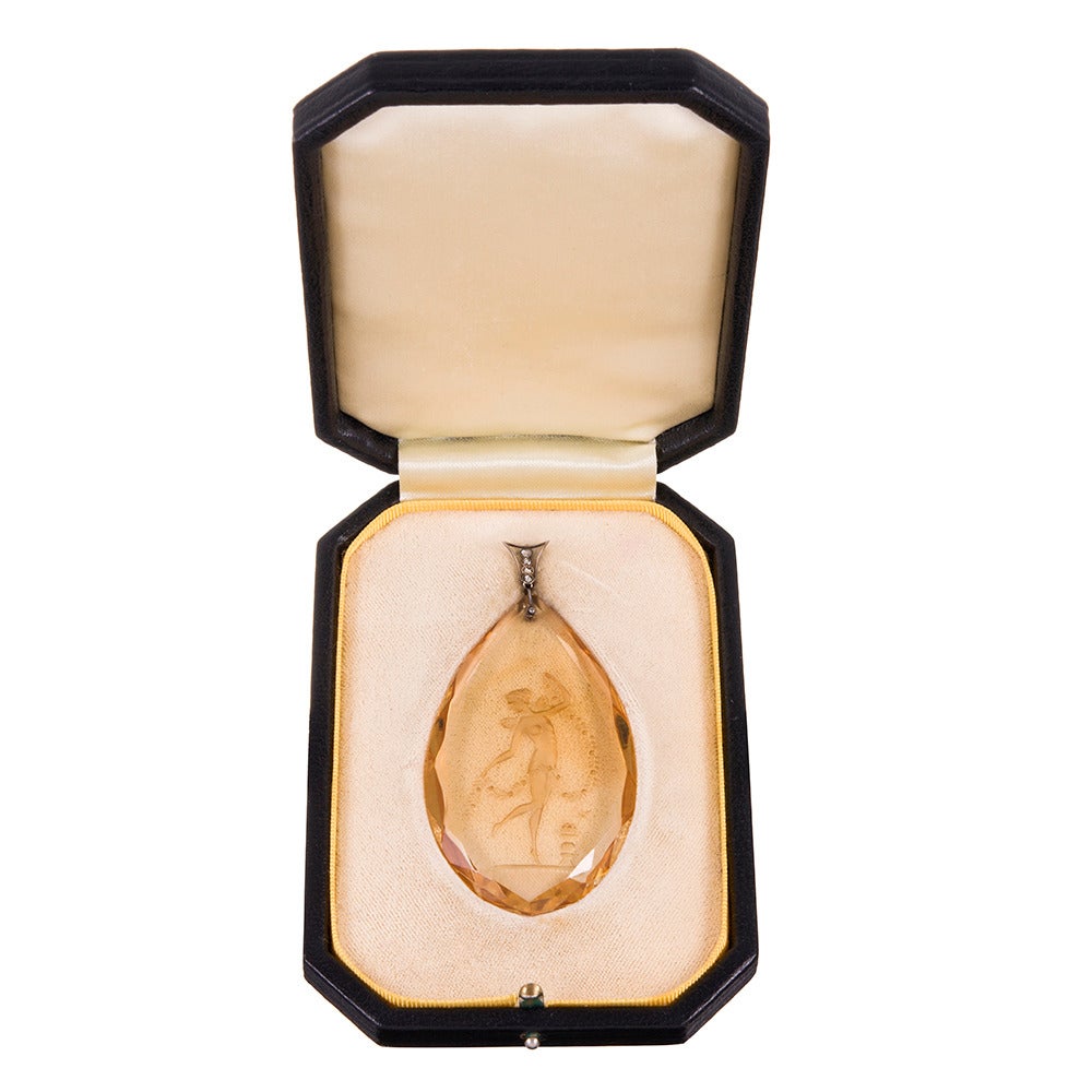 Antique feminine finery: a giant pear-shaped pendant of citroen, carved from the back and depicting a winged lady in frolic. Measuring 3 1/8 inches tall and finished with a bale, decorated with four rose cut diamonds. Offered in the original