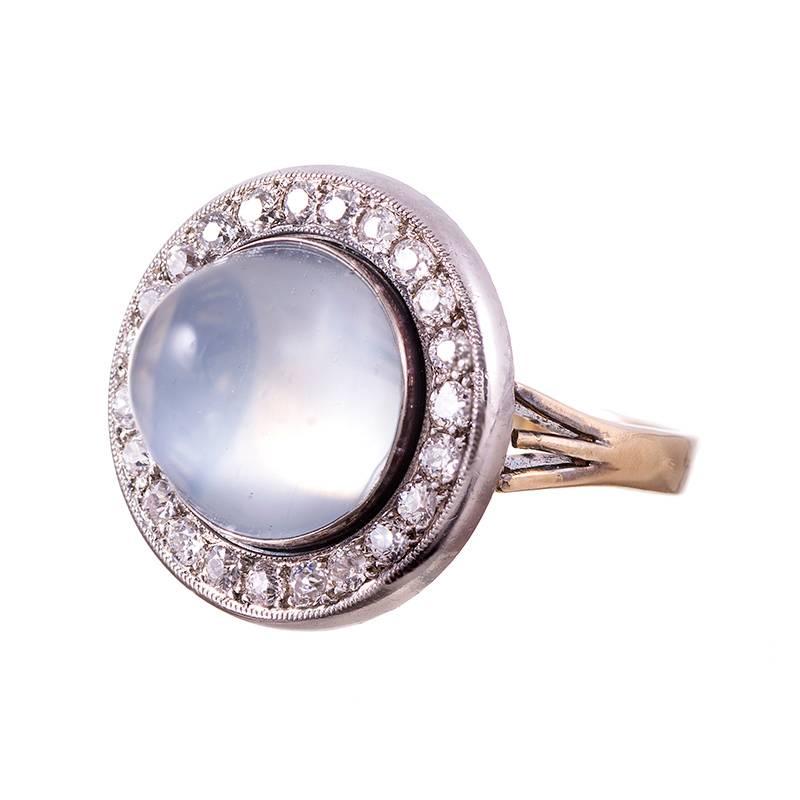 Set in platinum and 14k rose gold, this art deco rendering of a classic cluster design displays a cabochon cut moonstone sitting in a frame of old European cut diamonds. The moonstone exhibits a strong blue flash and alluring opalescence, drawing