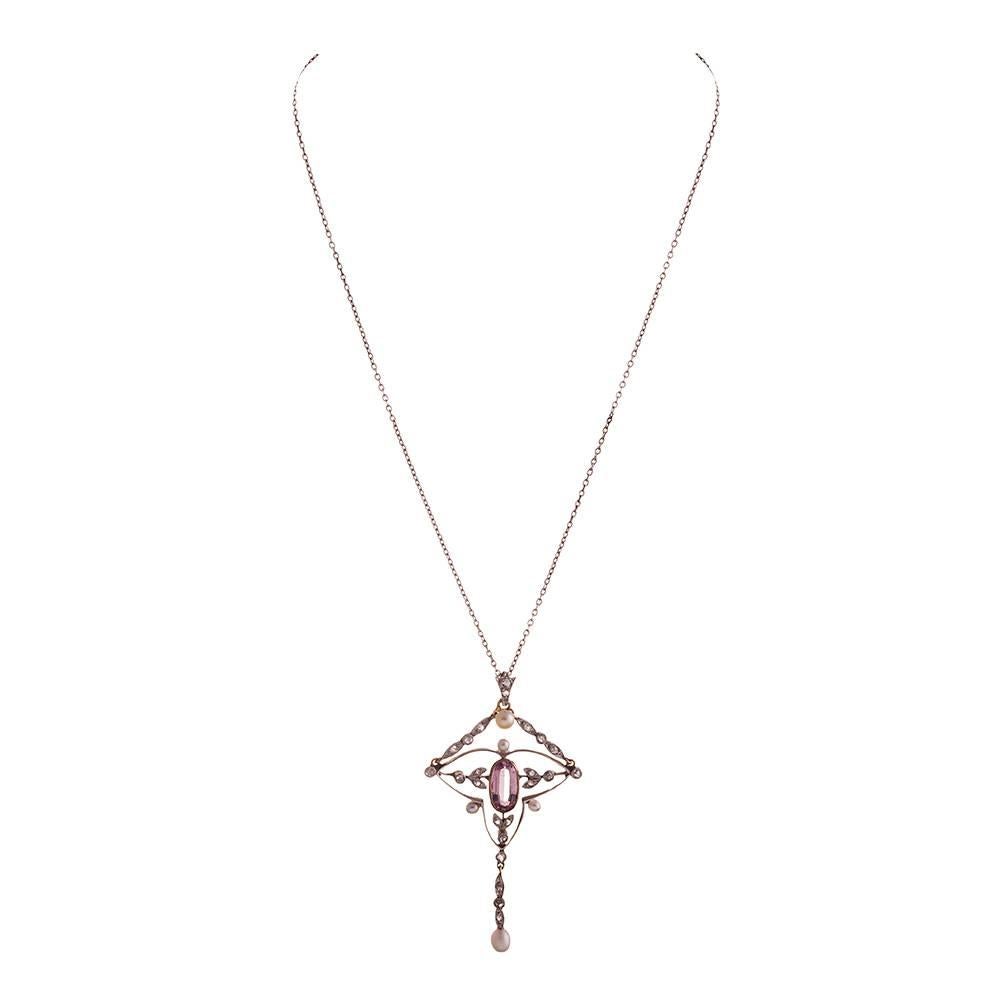Platinum over yellow gold necklace displaying classic Edwardian femininity with a precious pink topaz framed in a border of diamond-studded platinum leaves and pearls speckled throughout. Measuring a hint over 2 inches long and a whisper over 1 inch