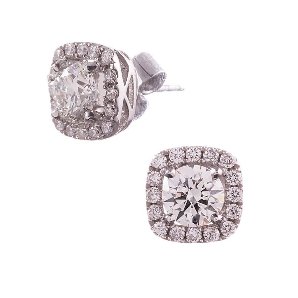 18 karat white gold diamond studs with a cushion shaped diamond halo framing each stone. The center diamonds are GIA graded J color and Si1 clarity, weighing 1.20 carats combined. The thirty-two diamond accent stones weigh .41 carats in total. These